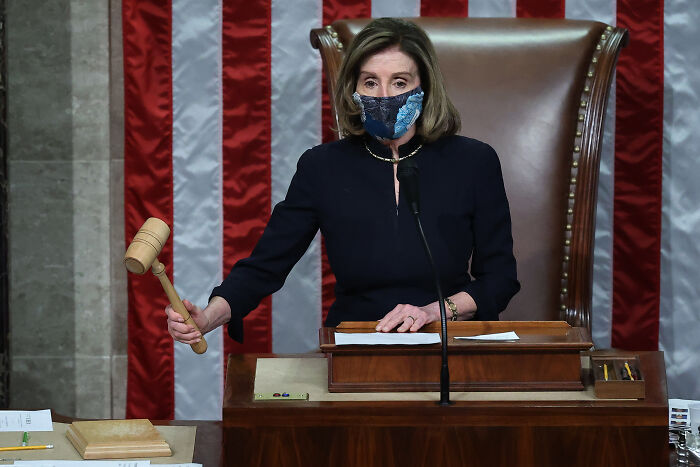 Nancy Pelosi holding a gavel in Congress chamber, wearing a mask during an official session at the podium. Nancy Pelosi holding a gavel in Congress chamber, wearing a mask during an official session at the podium.