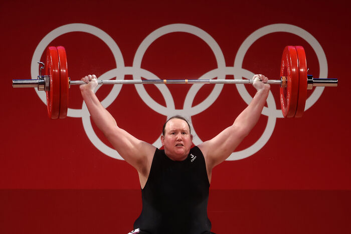 Weightlifter lifting a barbell at the Olympics, related to transgender and DSD competitors ban discussion.