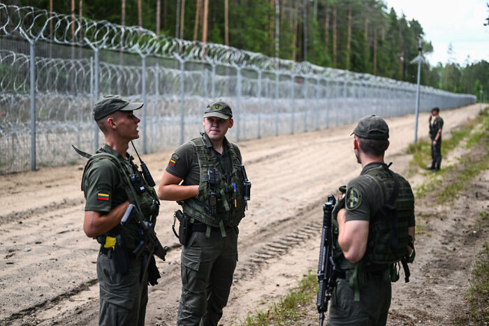 Border patrol officers in uniform standing by a barbed wire fence representing surveillance states and migration control. Border patrol officers in uniform standing by a barbed wire fence representing surveillance states and migration control.