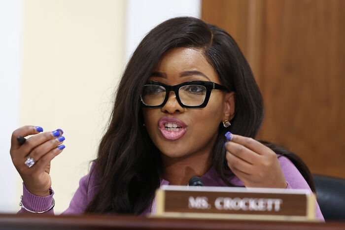 Jasmine Crockett speaking passionately during a congressional hearing, wearing black glasses and a purple outfit.