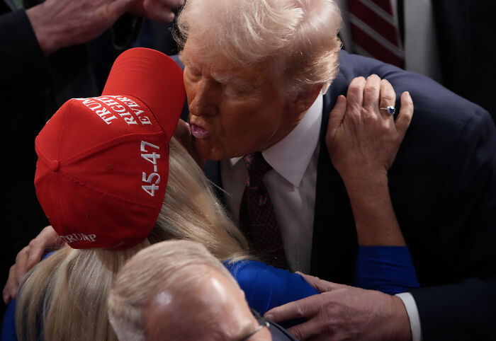 Donald Trump embracing a supporter wearing a red Make America Great Again hat at a political event.