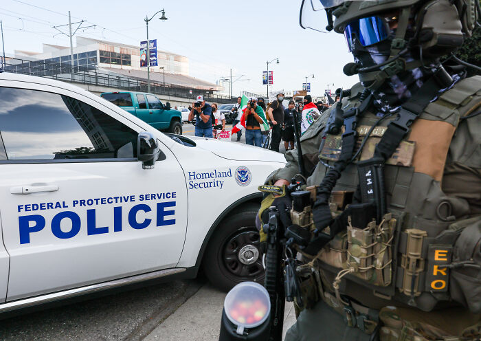 Heavily armed federal protective service police officer near Homeland Security vehicle during ICE raids protest. Heavily armed federal protective service police officer near Homeland Security vehicle during ICE raids protest.