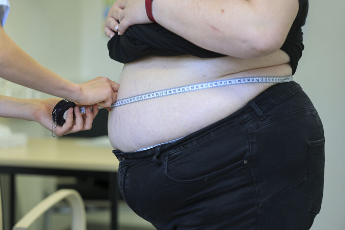 Measuring waist of overweight person illustrating Trump obesity ban blocking foreigners from entering U.S.