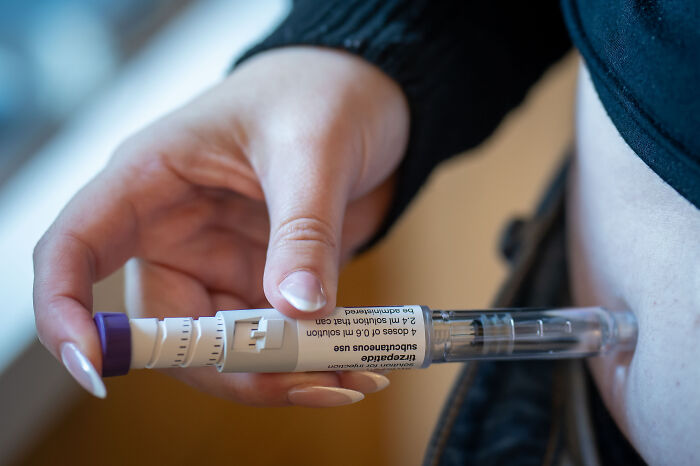 Person holding an injection pen near their abdomen, illustrating obesity and health concerns linked to Trump obesity ban policy.