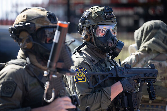 Federal agent in tactical gear holding a rifle, wearing a gas mask during a law enforcement operation. Federal agent in tactical gear holding a rifle, wearing a gas mask during a law enforcement operation.