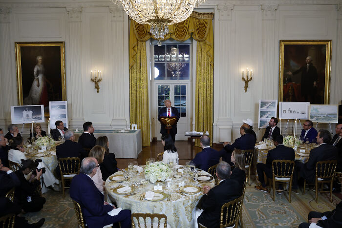 Donald Trump speaking at a formal event in the White House with guests seated at decorated round tables.