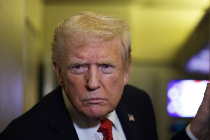 Donald Trump wearing a dark suit and red tie, looking serious amid rising pressure over Epstein files release.