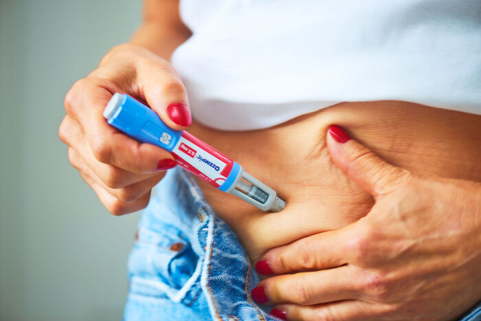 Close-up of hands with red nails using an injection pen on skin, unrelated to Donald Trump’s face or fainting incident. Close-up of hands with red nails using an injection pen on skin, unrelated to Donald Trump’s face or fainting incident.