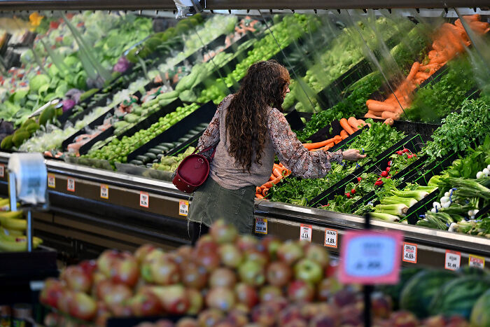 Woman shopping for fresh vegetables in grocery store, illustrating rising food costs affecting MAGA fans.