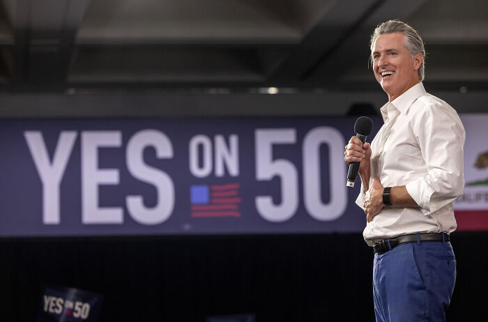 Man speaking at a political event with a Yes on 50 sign in the background, related to the battle for house seats.
