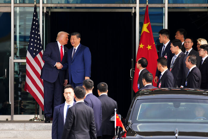 Donald Trump shaking hands with Xi Jinping outside a building, with officials and flags of the US and China present. Donald Trump shaking hands with Xi Jinping outside a building, with officials and flags of the US and China present.