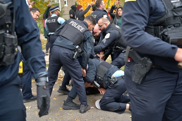 Several police officers restraining a person on the ground during a public protest or confrontation scene outdoors. Several police officers restraining a person on the ground during a public protest or confrontation scene outdoors.