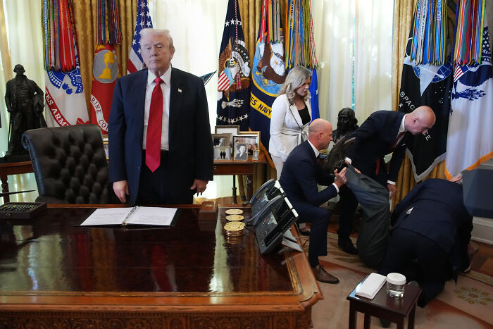Donald Trump standing with a serious expression while a man faints and is helped by others behind him in the Oval Office. Donald Trump standing with a serious expression while a man faints and is helped by others behind him in the Oval Office.