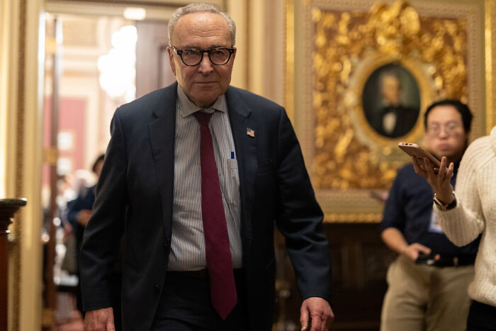 Senator walking in hallway wearing glasses and suit, symbolizing senators reaching deal to end government shutdown.
