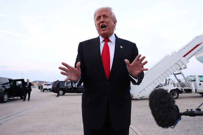 Former president Trump speaking at an airport with media, related to personality cult and Republican Party rename proposal.