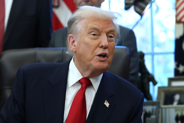 Former President Trump in the Oval Office, speaking during a meeting while wearing a dark suit and red tie. Former President Trump in the Oval Office, speaking during a meeting while wearing a dark suit and red tie.