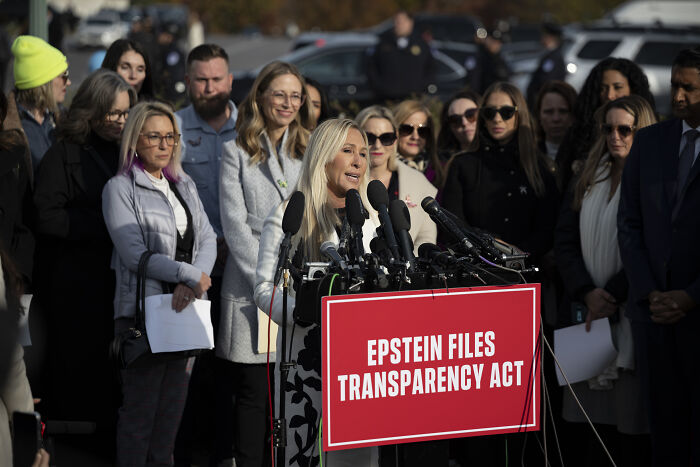 Woman speaking at podium with Epstein Files Transparency Act sign, surrounded by supporters during outdoor press event. Woman speaking at podium with Epstein Files Transparency Act sign, surrounded by supporters during outdoor press event.