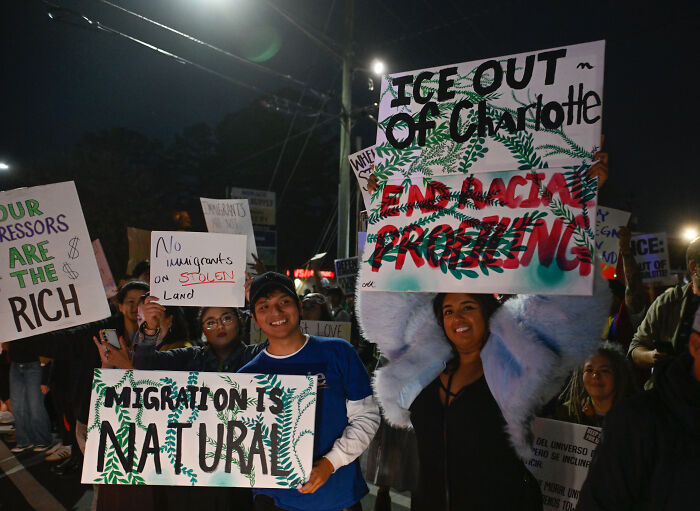 Protesters holding signs against ICE raids and advocating for migration rights during a nighttime demonstration. Protesters holding signs against ICE raids and advocating for migration rights during a nighttime demonstration.