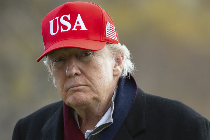 Donald Trump wearing a red USA hat, outdoors with a serious expression, related to New York skyscraper battle history. Donald Trump wearing a red USA hat, outdoors with a serious expression, related to New York skyscraper battle history.