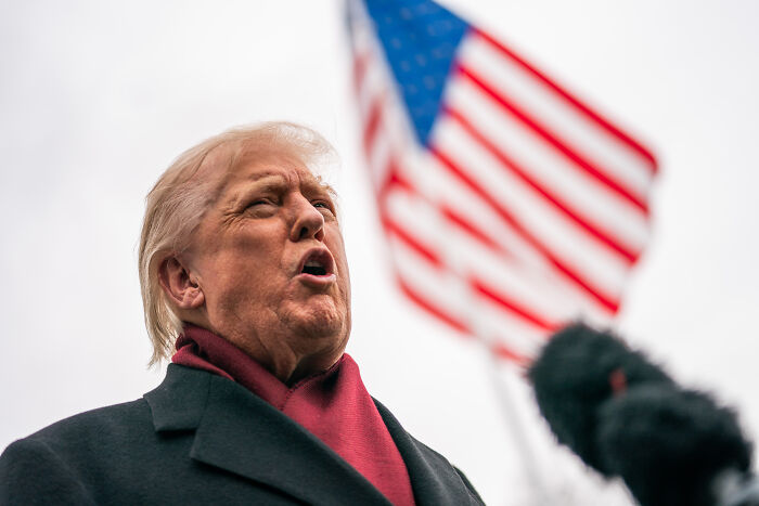 Donald Trump speaking forcefully outdoors with an American flag behind him during a Republican party event.