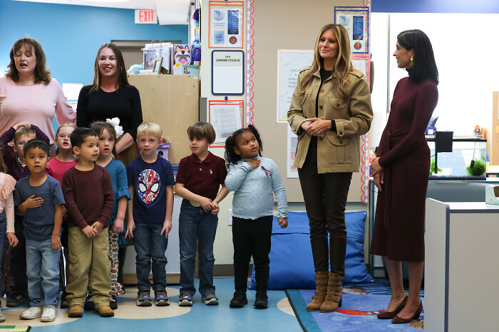 Melania Trump standing with children and staff at a school, sparking public backlash over dystopian troops address.