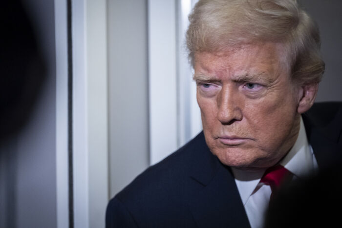 Former President Trump in a dark suit and red tie with a serious expression amid controversy over transparency and comments on female reporter