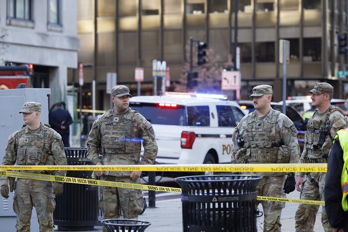 National Guard members stand behind police tape at a D.C. shooting scene with police vehicles in the background. National Guard members stand behind police tape at a D.C. shooting scene with police vehicles in the background.