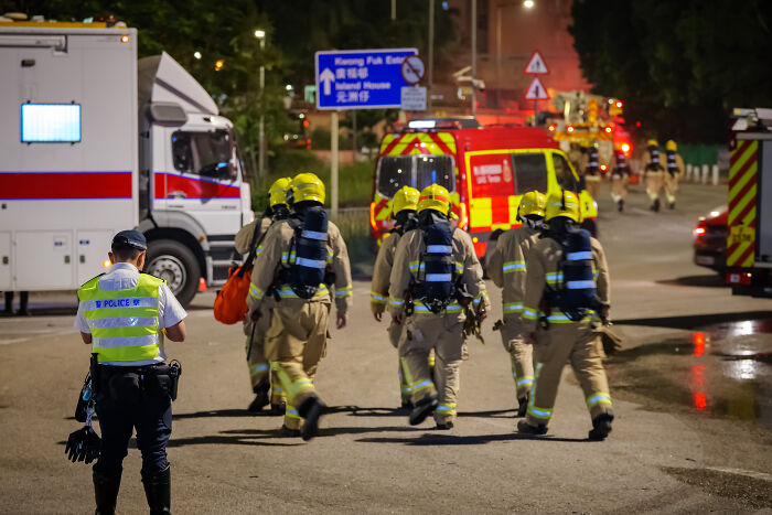 Firefighters and emergency personnel responding to Hong Kong apartment complex fire as fatalities rise, officials on site at night.
