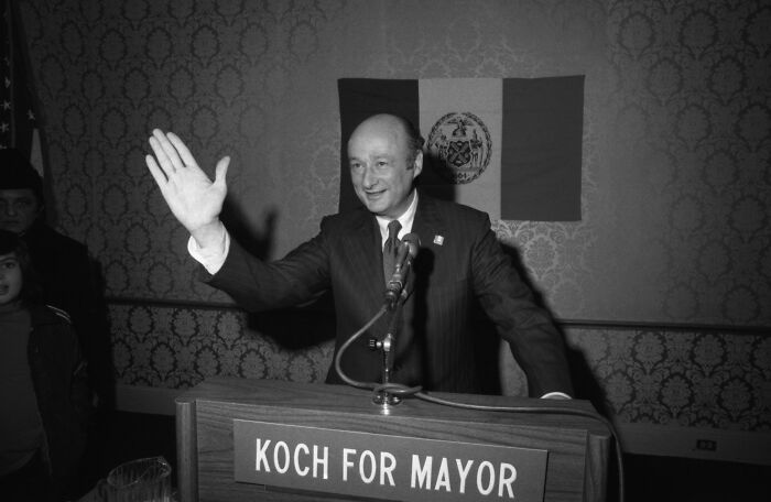 Black and white photo of a politician at a podium with Koch for Mayor sign, related to Trump piggy insult New York skyscraper battle. Black and white photo of a politician at a podium with Koch for Mayor sign, related to Trump piggy insult New York skyscraper battle.