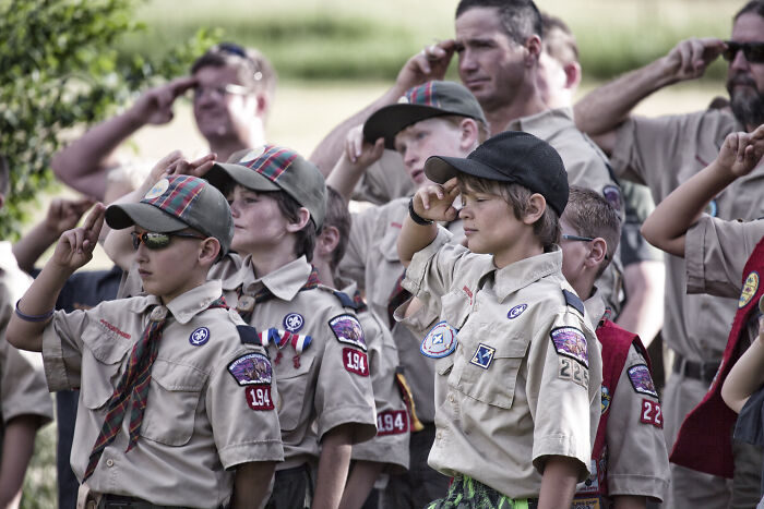 Boy Scouts in uniform saluting during an outdoor ceremony reflecting ties with Boy Scouts and genderless controversy.