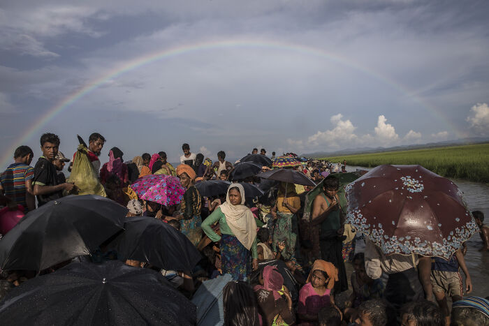 Crowd of migrants with umbrellas under a rainbow, illustrating migration control in surveillance states and data clouds. Crowd of migrants with umbrellas under a rainbow, illustrating migration control in surveillance states and data clouds.