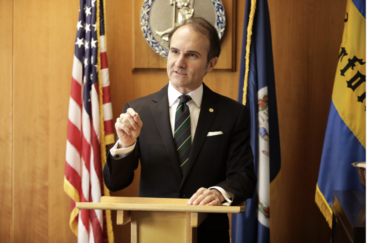 Man in suit speaking at a podium with American and Virginia state flags in the background about parents jailed and baby stroller fall case Man in suit speaking at a podium with American and Virginia state flags in the background about parents jailed and baby stroller fall case