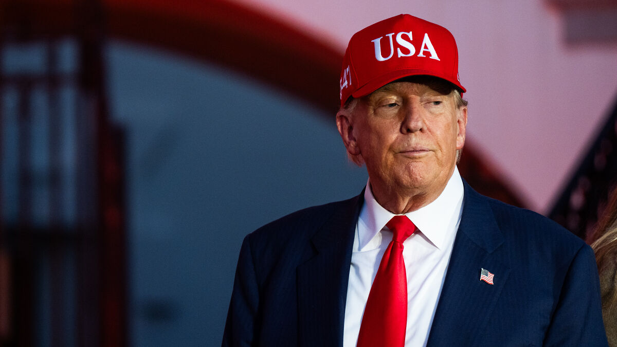 Former President Trump wearing a red USA hat and red tie, reacting amid questions about pardoning crypto king linked to his sons.