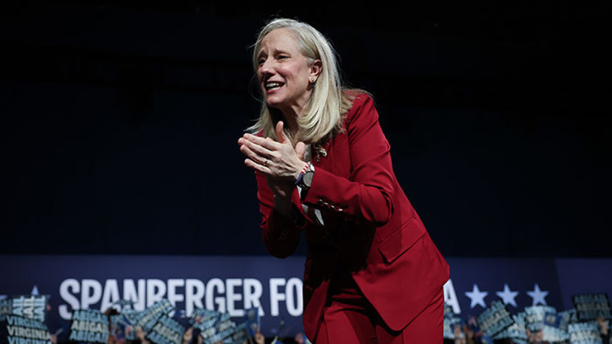 Woman in red suit applauding at a political event signaling Virginia turns blue in a sweeping victory against Trump.