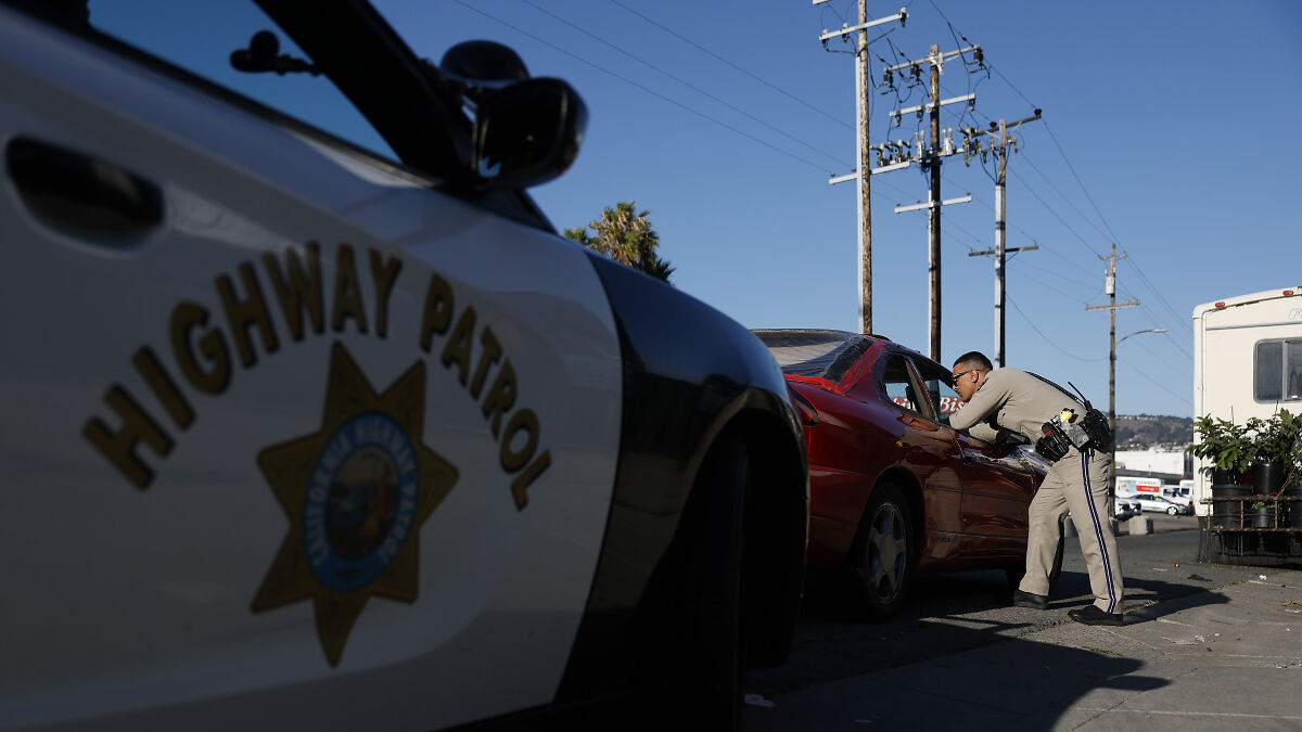 California Highway Patrol officer leaning into a red car during traffic enforcement on a sunny day.