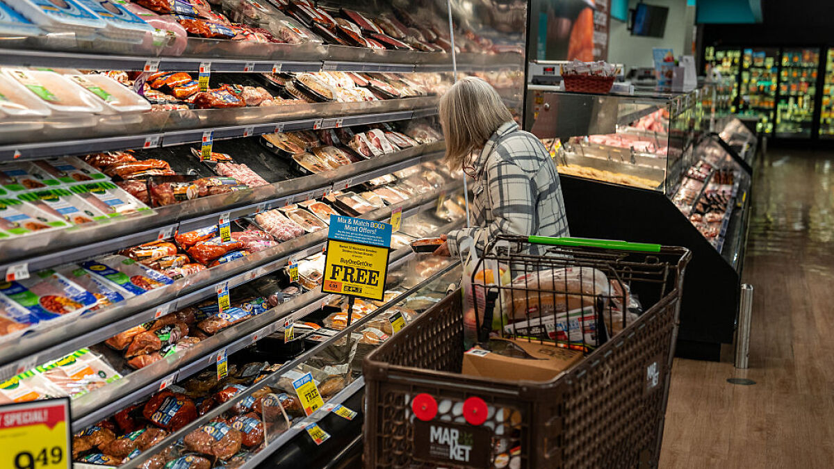 Woman with shopping cart selecting groceries in store, illustrating Americans living paycheck to paycheck challenges.
