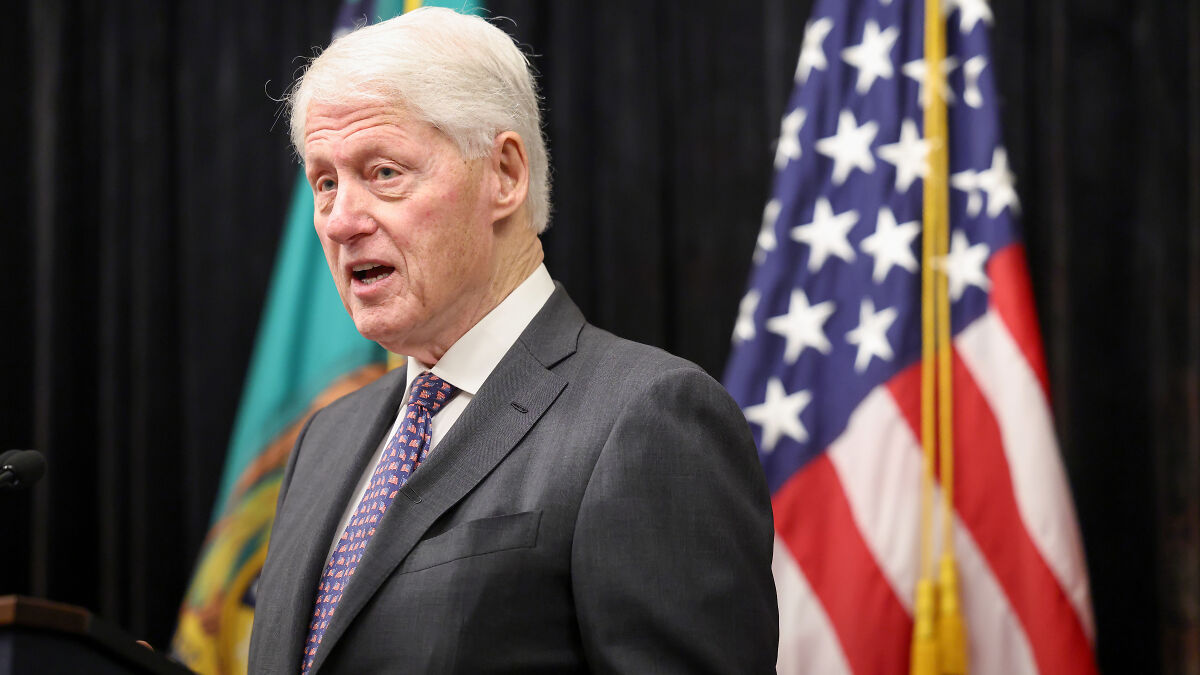 Older man in suit speaking at a podium with American flag in the background, related to Epsteinu2019s brother email topic.