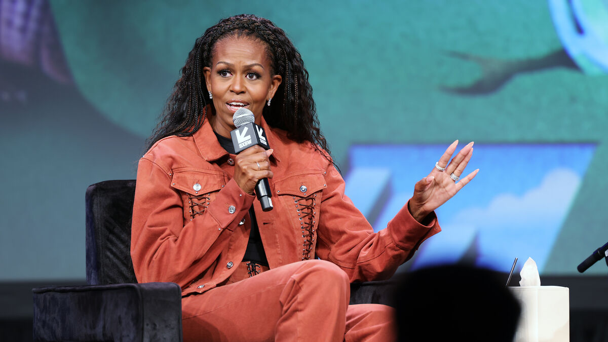 Michelle Obama speaking at an event, holding a microphone, sharing reasons for not pursuing presidential run.