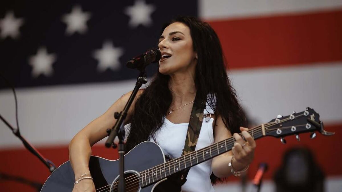 Country musician singing and playing guitar on stage with American flag backdrop, linked to FBI Director Kash Patel.
