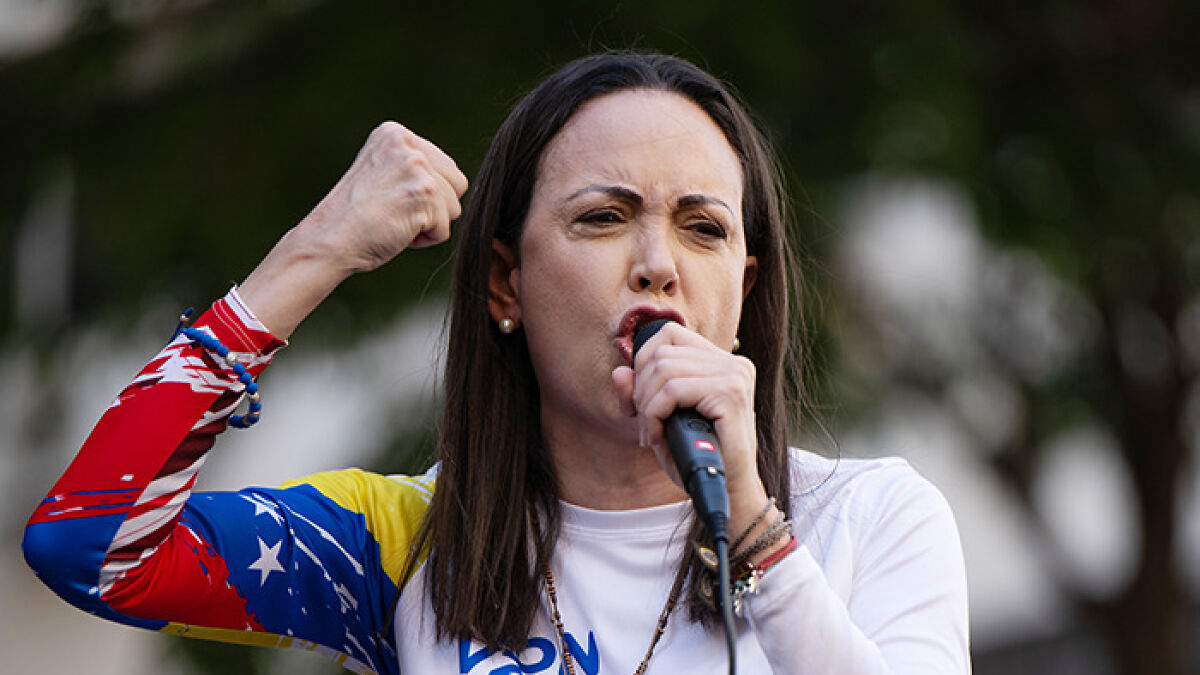 Maru00eda Corina Machado speaking passionately into a microphone, raising a fist while advocating military intervention.