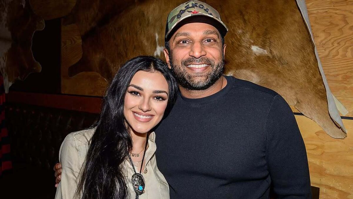 Kash Patel smiling with a woman indoors, both posing closely in a casual setting with wood panel background