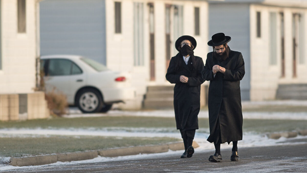 Two men in traditional attire walking outside near a building in a scene related to Lev Tahor sect police rescue.