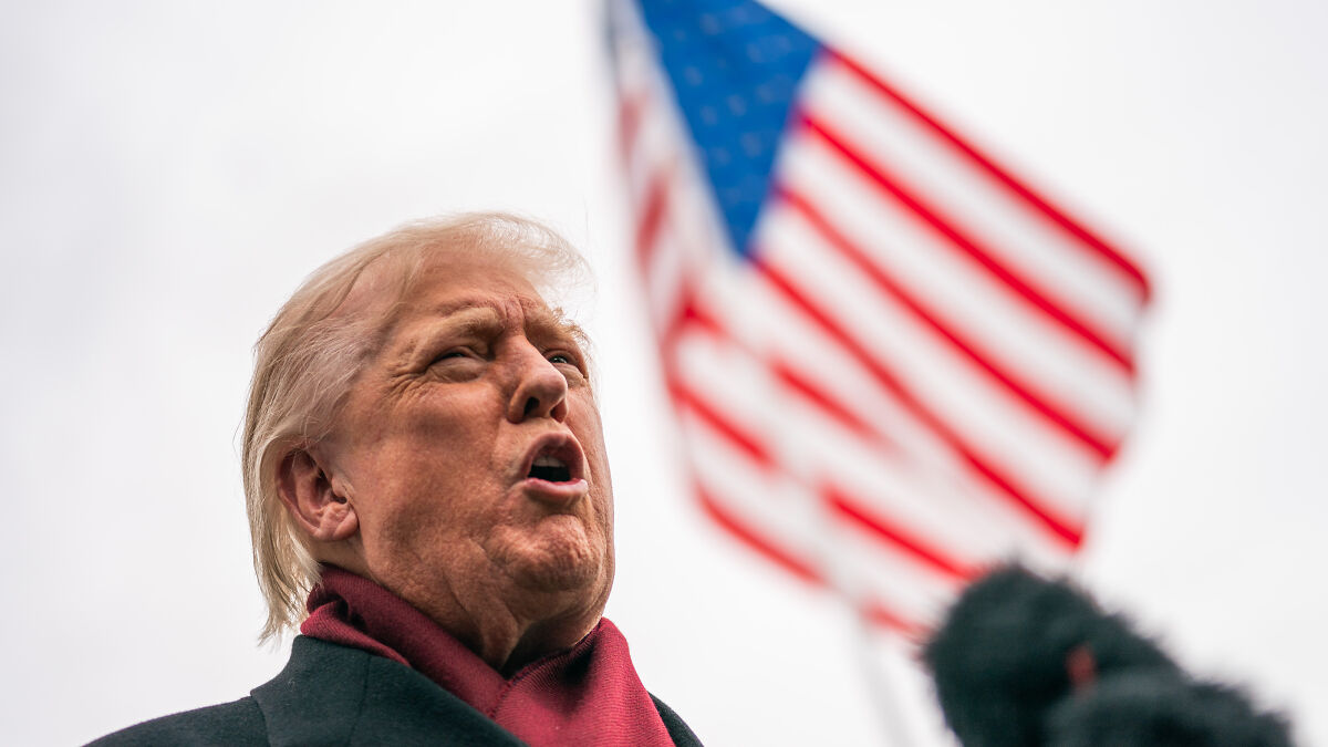 Former Trump supporter speaking passionately outdoors with American flag blurred in the background in 2025.