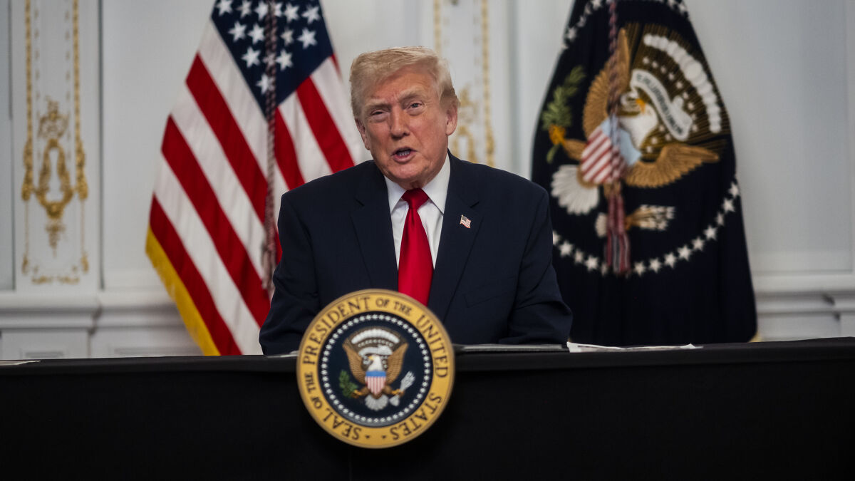 Former president speaking at a podium with the presidential seal in front of U.S. and presidential flags indoors.