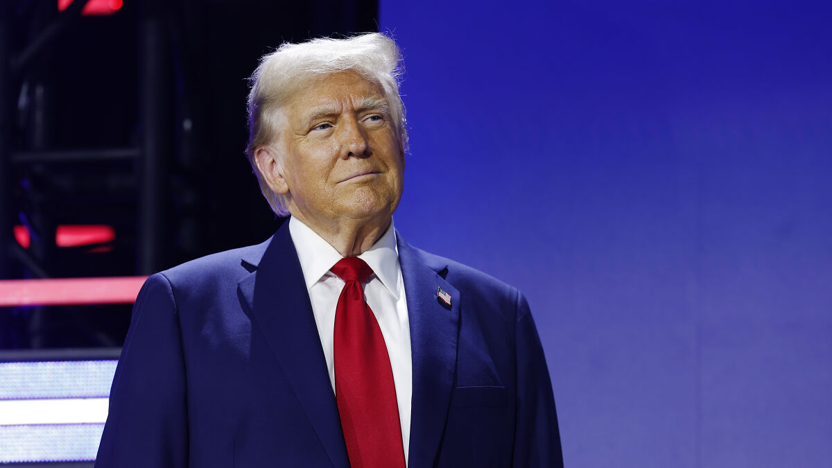 Donald Trump in a suit with red tie, speaking at an event discussing Coast Guard ships redesign and aesthetics.
