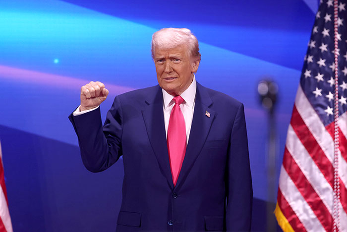 Donald Trump raising fist at a podium with American flags in the background during a political event. Donald Trump raising fist at a podium with American flags in the background during a political event.