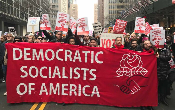 Protesters holding a red banner for Democratic Socialists of America during a rally in a city street. Protesters holding a red banner for Democratic Socialists of America during a rally in a city street.