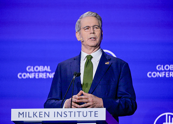 Man in suit and glasses speaking at Milken Institute event on new energy and G20 powers ahead with global conference backdrop. Man in suit and glasses speaking at Milken Institute event on new energy and G20 powers ahead with global conference backdrop.
