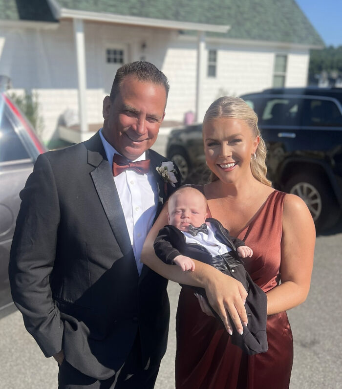 Karoline Leavitt in a red dress holding a baby, standing next to a man in a black tuxedo, smiling outdoors on a sunny day. Karoline Leavitt in a red dress holding a baby, standing next to a man in a black tuxedo, smiling outdoors on a sunny day.