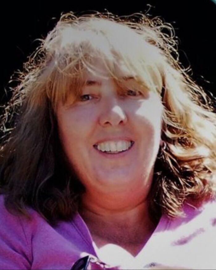 Woman, 64, smiling outdoors with sunlight on her face, related to boy 14 involved in home incident.